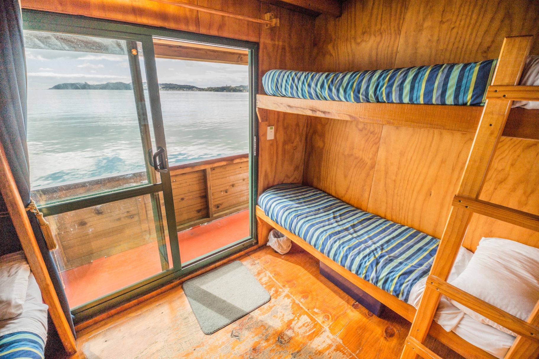 Classic shared bunk cabin onboard The Rock with bunk beds, ladder and Bay of Islands sea view through sliding door