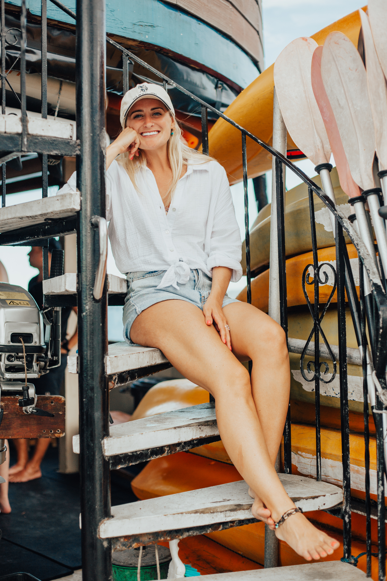 A crew member of The Rock smiling on the spiral staircase among stacked kayaks and paddles